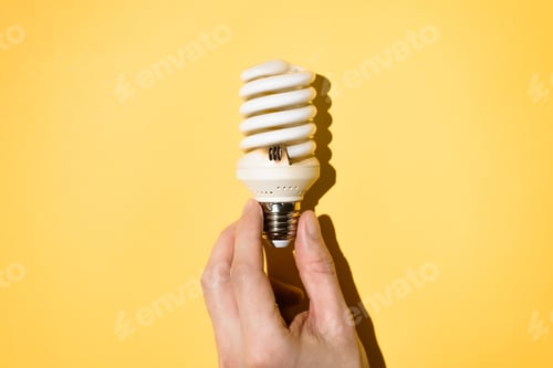 Preview: Male hand holding a light bulb on a yellow background, top view. Burnt out light bulb, flat lay