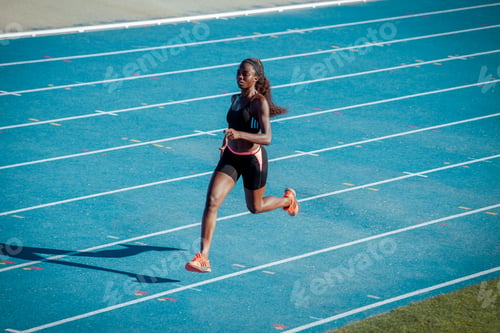 Preview: A black athlete of African origin trains her speed on a blue athletics track.