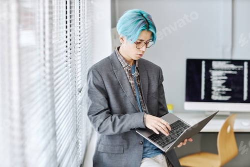 Preview: Asian young man using laptop sitting by window in office