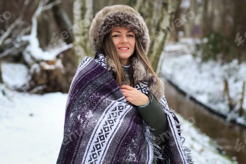 Preview: Photo a young woman wearing a cozy winter hat and wrapped in blanket on forest path.Millennial life.