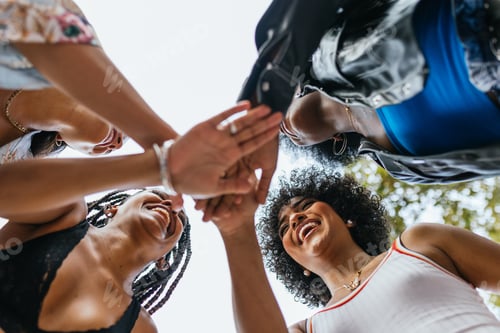 Preview: Group of diverse female friends sharing a joyous handshake outdoors on a sunny day.