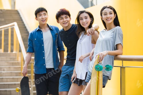Preview: Happy young Chinese friends holding skateboards standing together