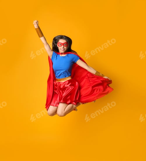 Preview: Confident young woman in superhero costume jumping on orange background
