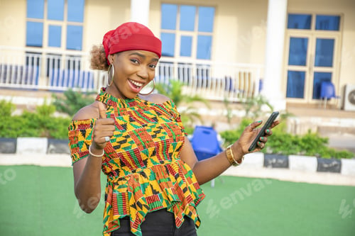 Preview: Pretty young African woman smiling and using her mobile phone outdoors