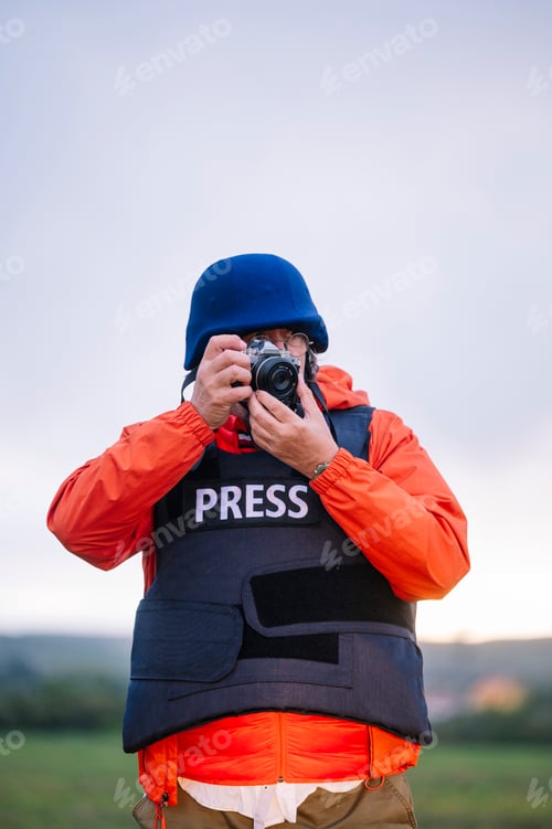 Preview: Reporter in bulletproof vest holding a camera.