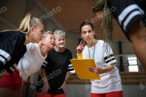 Preview: Female sport coach with clipboard discussing tactics with young and old women team training for
