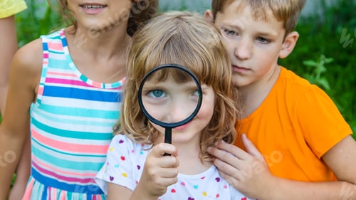 Preview: Children look at a magnifying glass on the nature. Selective focus.