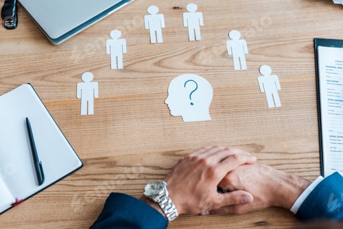 Preview: cropped view of recruiter with clenched hands near paper human shapes on table