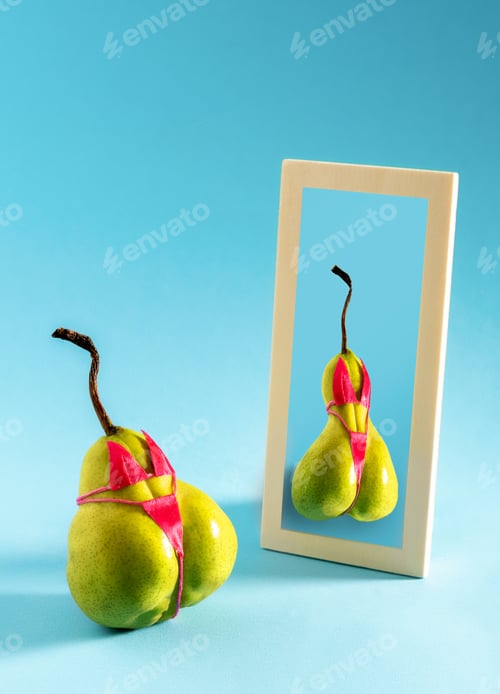 Preview: Pear looking at its reflection in mirror on blue background.