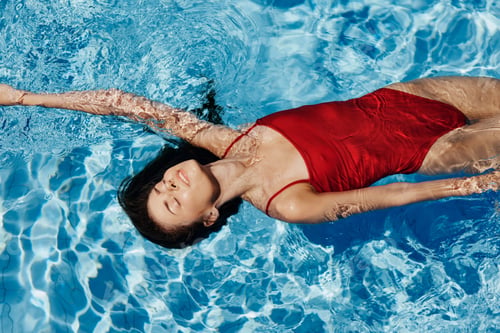 Preview: Young woman in the pool in a red swimsuit with a beautiful smile lying on the water and swimming in