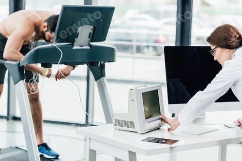 Preview: doctor looking at monitor while conducting endurance test with sportsman in gym
