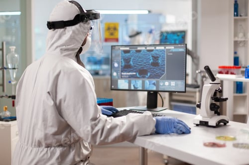 Preview: Scientist in protection suit typing on pc working in medical laboratory