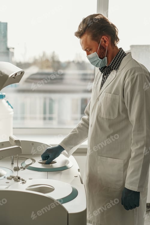 Preview: Male scientist in uniform and mask working in medical research laboratory use special equipment
