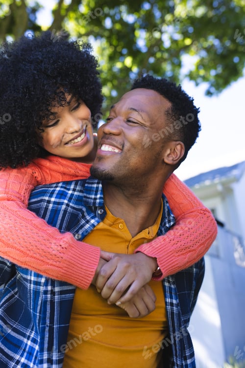Preview: Happy african american couple riding piggyback in sunny garden, copy space