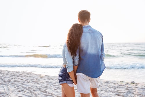 Vista previa: Back view of couple standing and holding hands on beach