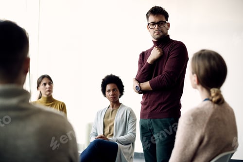Preview: Young man communicating with support group during therapy at community center.