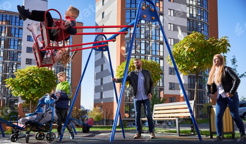 Preview: Happy family - father, mother and children having fun together on playground.