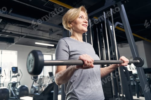 Preview: Joyful woman doing exercise with barbell in gym
