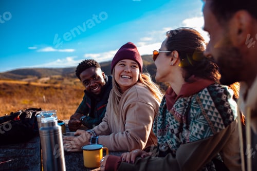 Vista previa: Group of friends sitting on the top of the hill at bench resting after hiking and drinking tea.