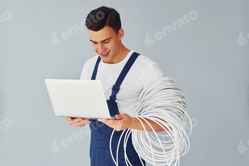 Preview: Uses laptop. Male worker in blue uniform standing inside of studio against white background
