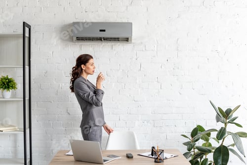 Preview: pretty businesswoman drinking water while standing near workplace under air conditioner