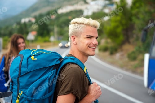 Preview: Concept of traveling alone. Young Caucasian man hitchhiking standing by road on sunny summer day