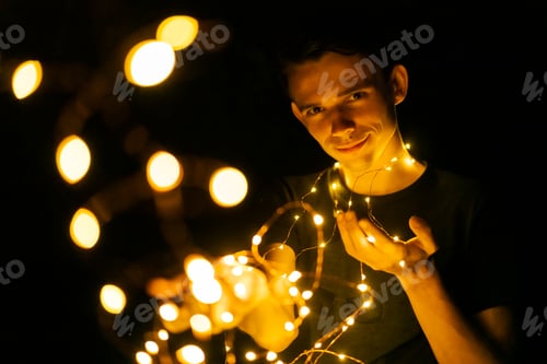 Preview: young guy at night holding glowing garlands in his hands, selective focus