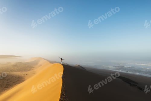 Preview: Woman walking on top of huge sand dune in Morocco Sahara desert. Beautiful warm sun light and mist