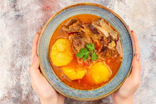 Preview: top view bozbash soup in a bowl in female hand on nude background azerbaijani cuisine