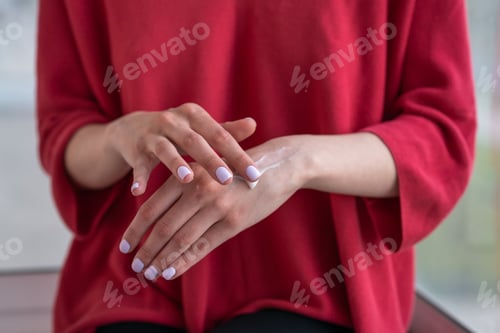 Preview: girl sits on the windowsill and applies cream on her hands