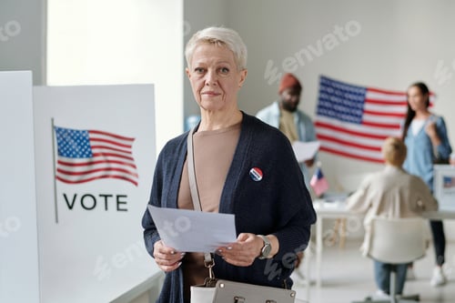 Preview: Confident mature blond female voter with ballot paper