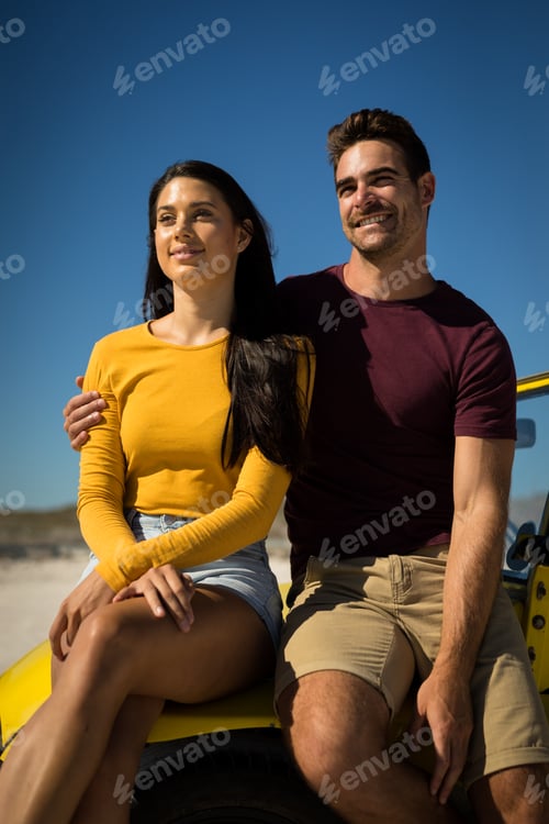 Preview: Happy caucasian couple woman sitting in beach buggy by the sea both looking ahead