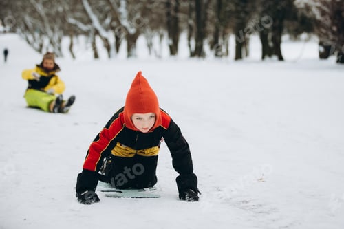 Preview: Young boy having fun sledding in snowy winter park