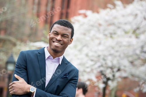 Preview: City life in spring. A man in a blue suit with arms folded, in a city park.