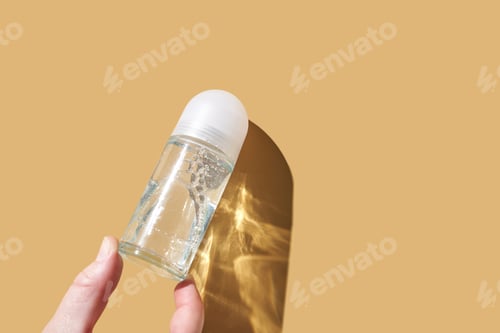 Vista previa: Hand holding clear roll-on deodorant against minimalistic beige background