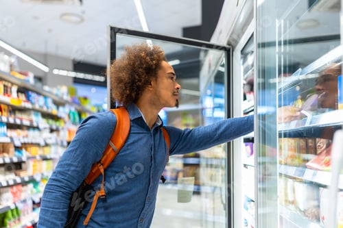 Preview: Young man choosing frozen food in supermarket freezer