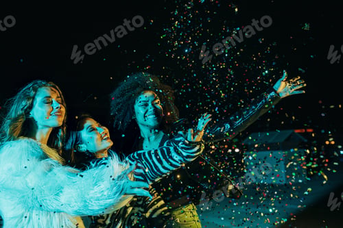 Preview: Three happy girls throwing confetti while standing on the roof under neon lights