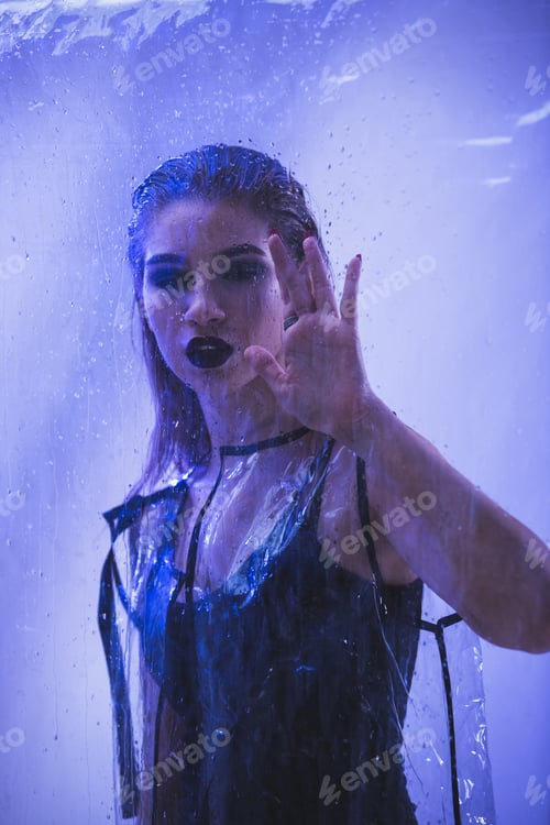 Preview: Fashionable model with wet hair and dark lipstick dressed in black swimming suit and transparent