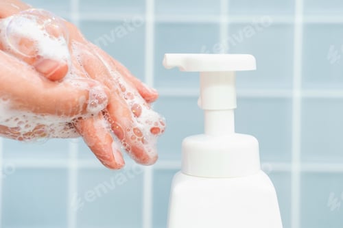 Preview: Hands squeeze liquid soap with foam from white bottle on blue tile background.