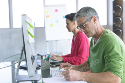 Preview: Side view of Multi-ethnic business people working on computer at desk in modern office