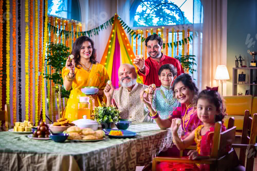 Preview: Portrait of happy Indian family in traditional outfit celebrating Diwali at home eating food