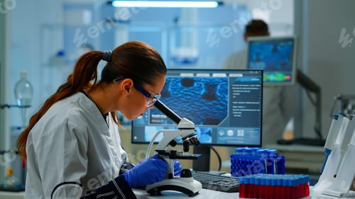 Preview: Scientist looking at biological samples under microscope typing on pc