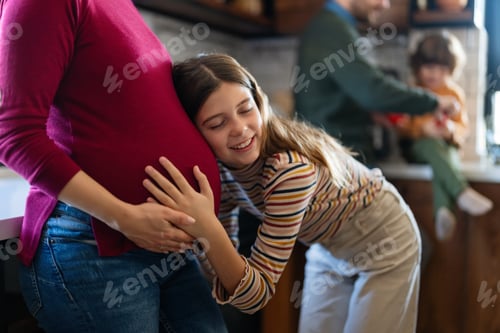 Preview: Happy daughter hugging belly her expecting mother at home. Excited girl listening to baby movement