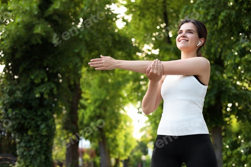 Preview: Young woman with wireless earphones doing morning exercise outdoors