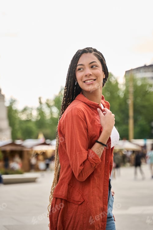 Preview: Young latina woman smiling and walking in city with braids