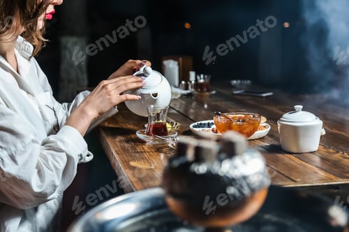 Preview: side view a girl pours tea into an armudu glass with nuts raisins and lemon wedges with jam
