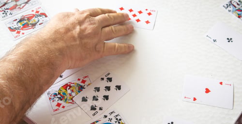 Preview: Close-up of a man's hand laying out playing cards on a white table, gambling concept