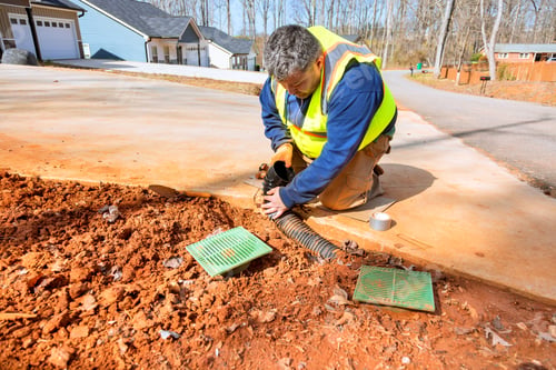 Preview: Worker repairs drainage system near residential area on sunny day