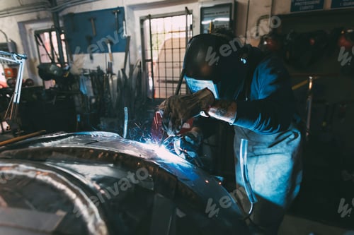 Preview: Metalworker in welding mask soldering metal in forge workshop