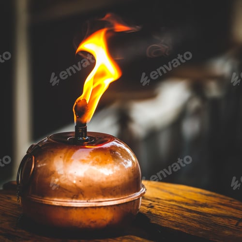 Preview: Closeup shot of a burning antique smudge pot on a wooden surface